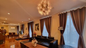 A modern living room with a black leather sofa, a wooden coffee table, and a chandelier. There is a dining area in the background with a table and chairs. - Chez Moi Bangkok Sukhumvit 26 Executive Residence (888) (Klong Toey)