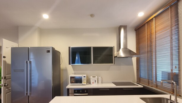 A modern kitchen with a stainless steel refrigerator, a microwave, and a built-in oven. There is a large island with a sink and a window with blinds. - Chez Moi Bangkok Sukhumvit 26 Executive Residence (888) (Klong Toey)