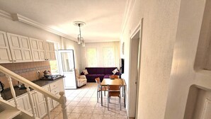 A kitchen with white cabinets, a dining area with a wooden table and chairs, and a purple sofa. - Azure Ev Fethiye (Fethiye)