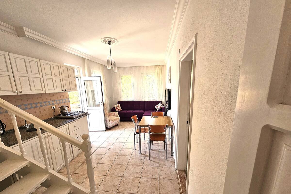 A kitchen with white cabinets, a dining area with a wooden table and chairs, and a purple sofa.