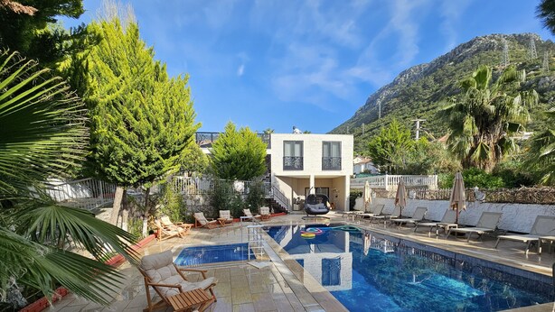 A pool area with lounge chairs, a clear blue pool, and a mountain backdrop. - Azure Ev Fethiye (Fethiye)