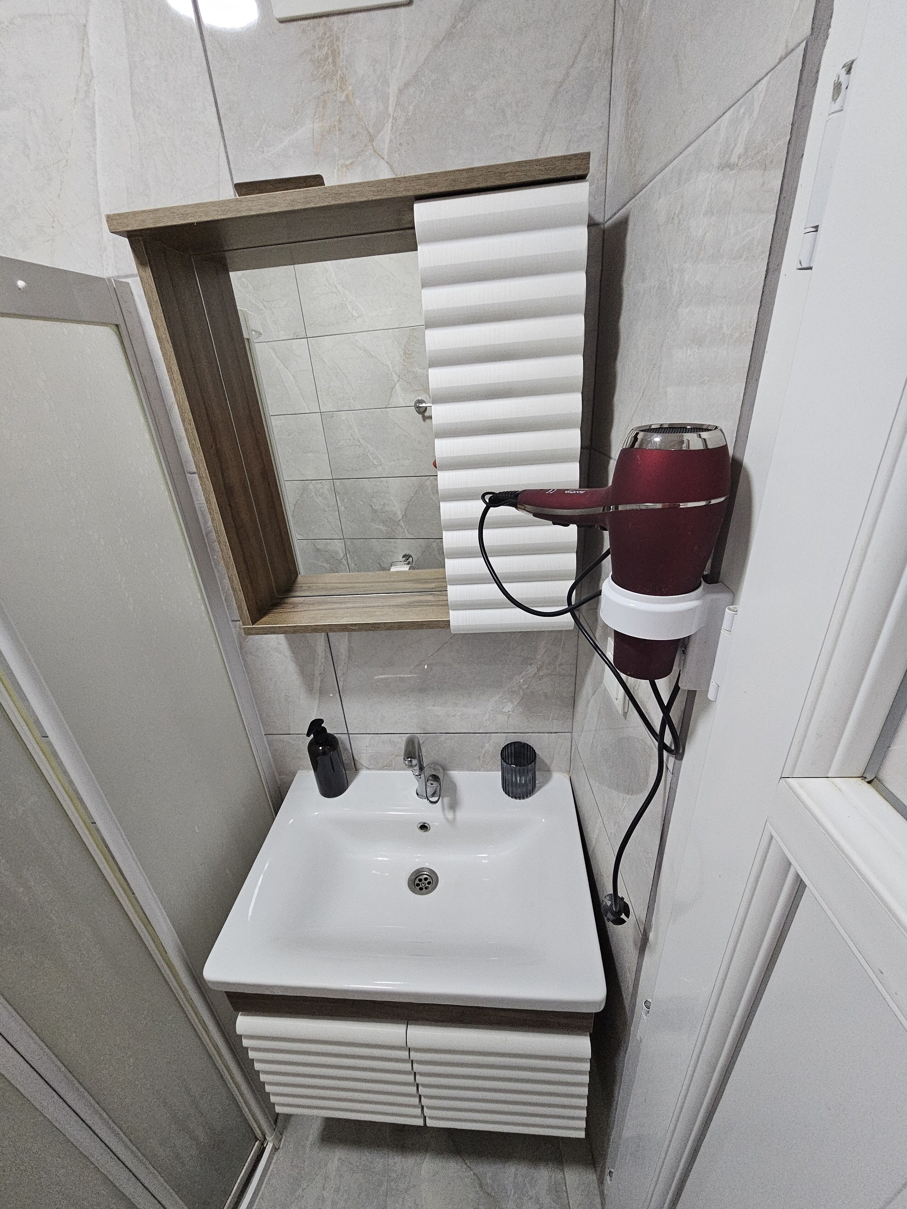 Un baño con un lavamanos blanco, un espejo y un secador de pelo rojo.