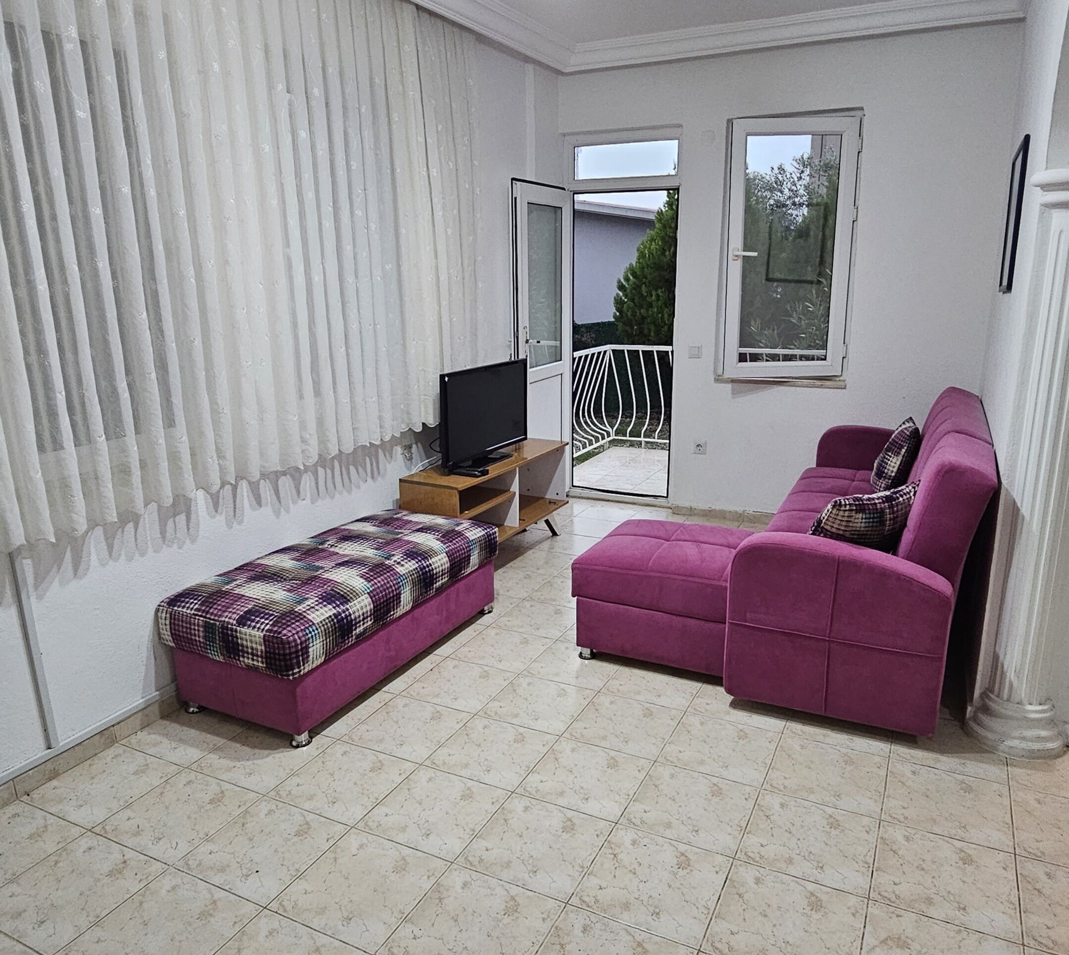 A living room with a sofa, ottoman, and TV on a wooden stand.