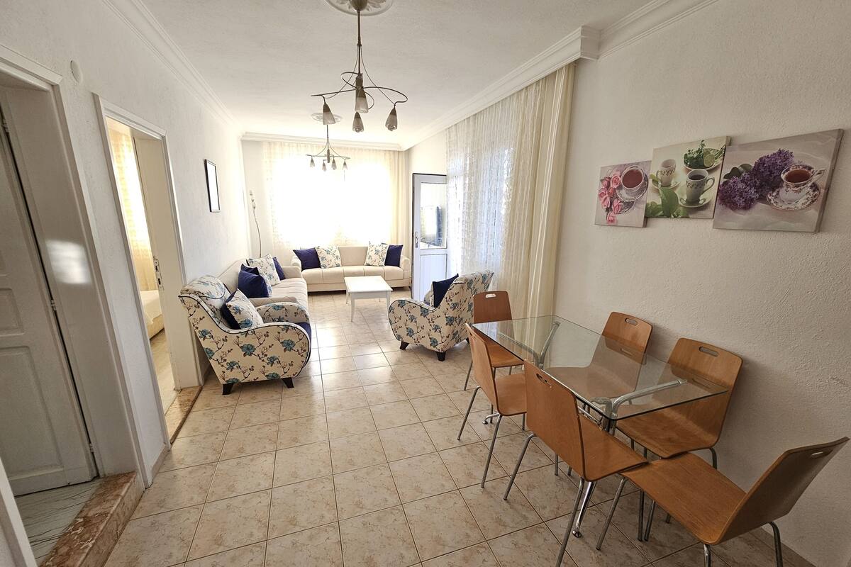 A spacious living area with a sofa set, a glass dining table, and a chandelier.
