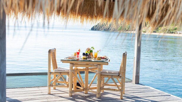 A wooden deck with a glass table and chairs overlooking a body of water. - The Seraya Resort Komodo (Labuan Bajo)