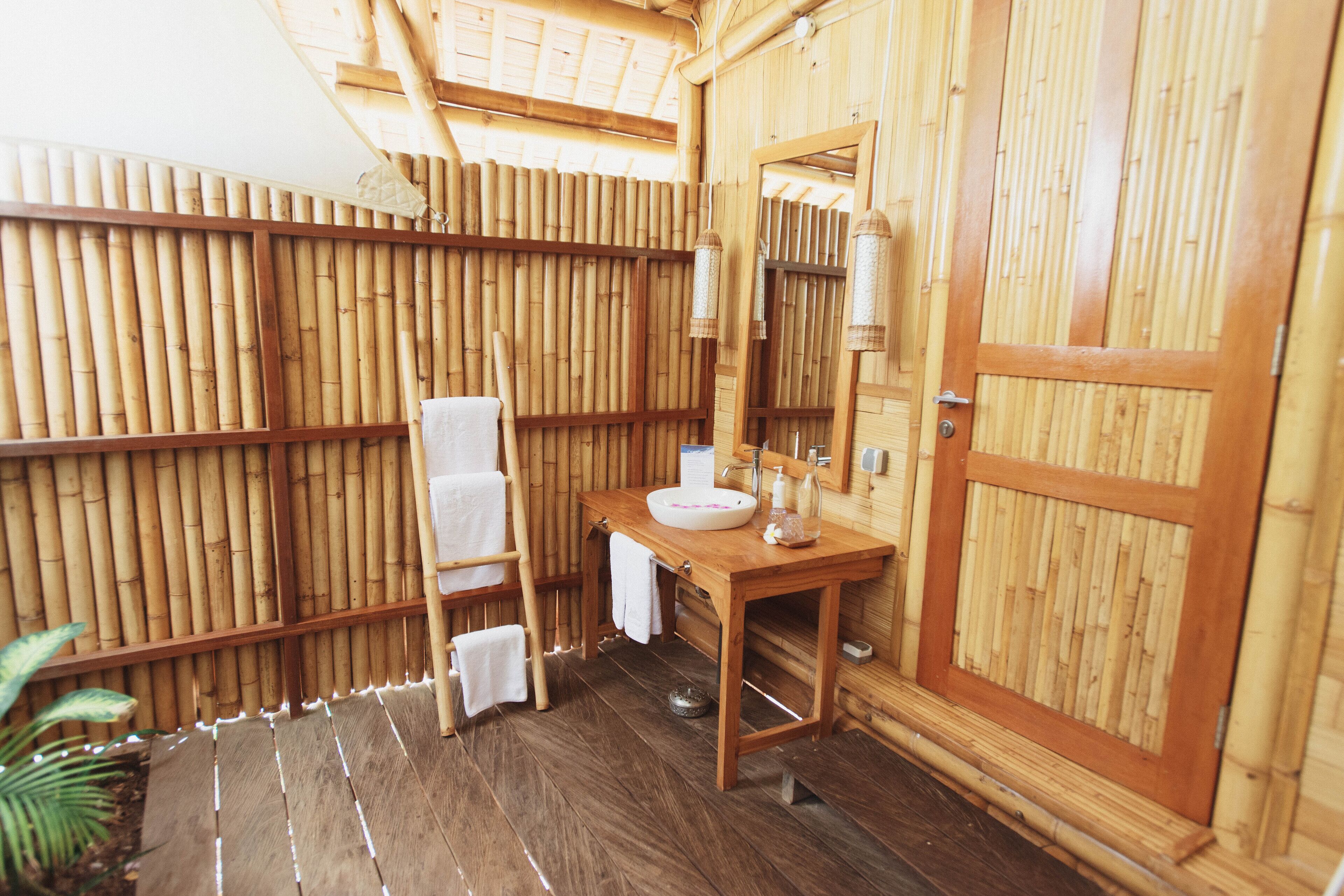 A bamboo-fenced bathroom with a wooden vanity, a sink, and a towel rack.