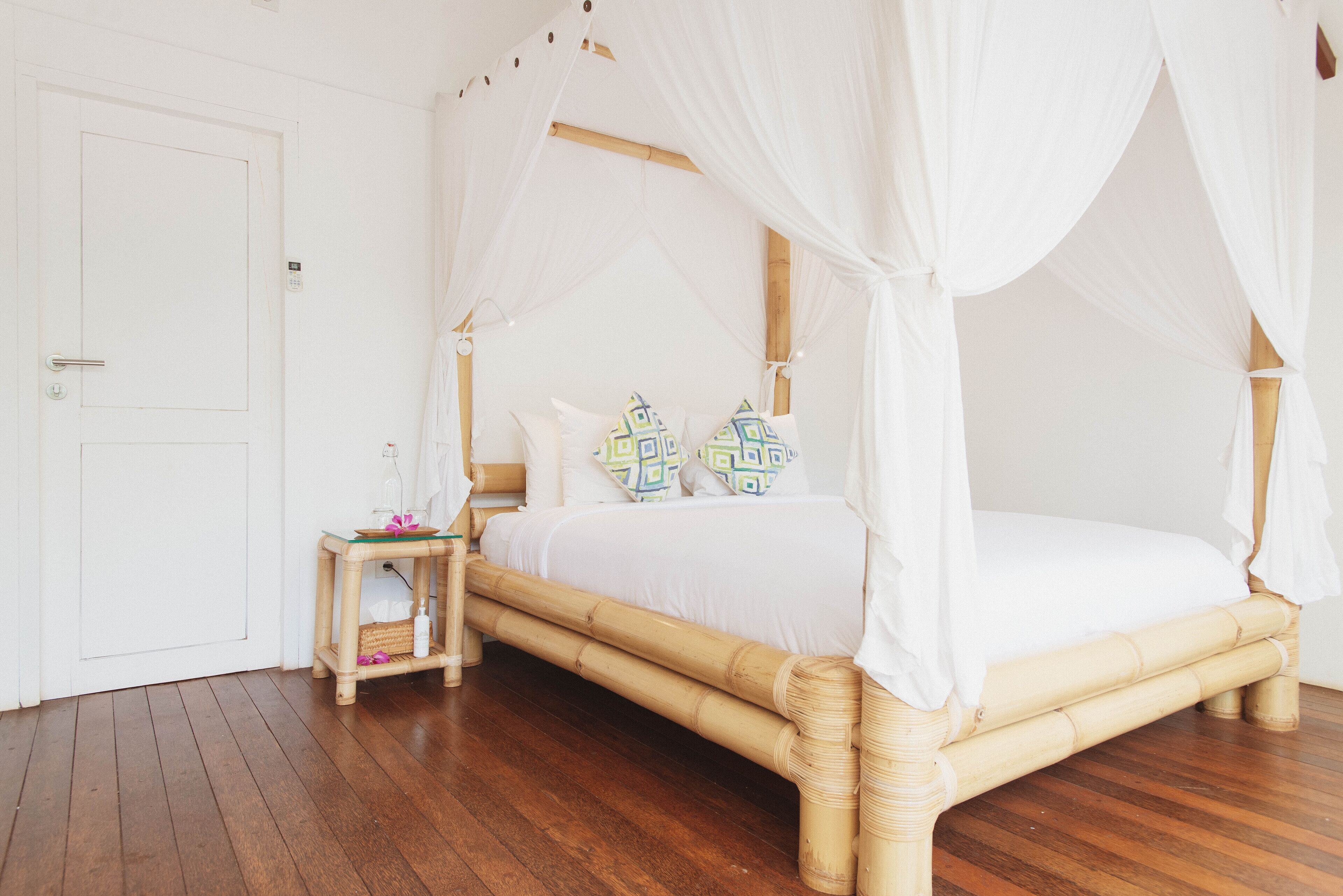 Una habitación con cama con dosel, una mesita de noche pequeña y suelo de madera.
