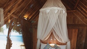 A room with a bed, a bedside table, and a view of the beach. - The Seraya Resort Komodo (Labuan Bajo)