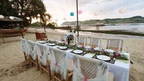 A beachside dining setup with a long table, chairs, and a view of the sea. - The Seraya Resort Komodo (Labuan Bajo)