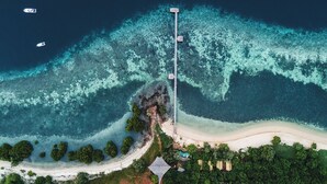 An aerial view of a coastal property with a long pier extending into the sea, surrounded by lush greenery and a sandy beach. - The Seraya Resort Komodo (Labuan Bajo)