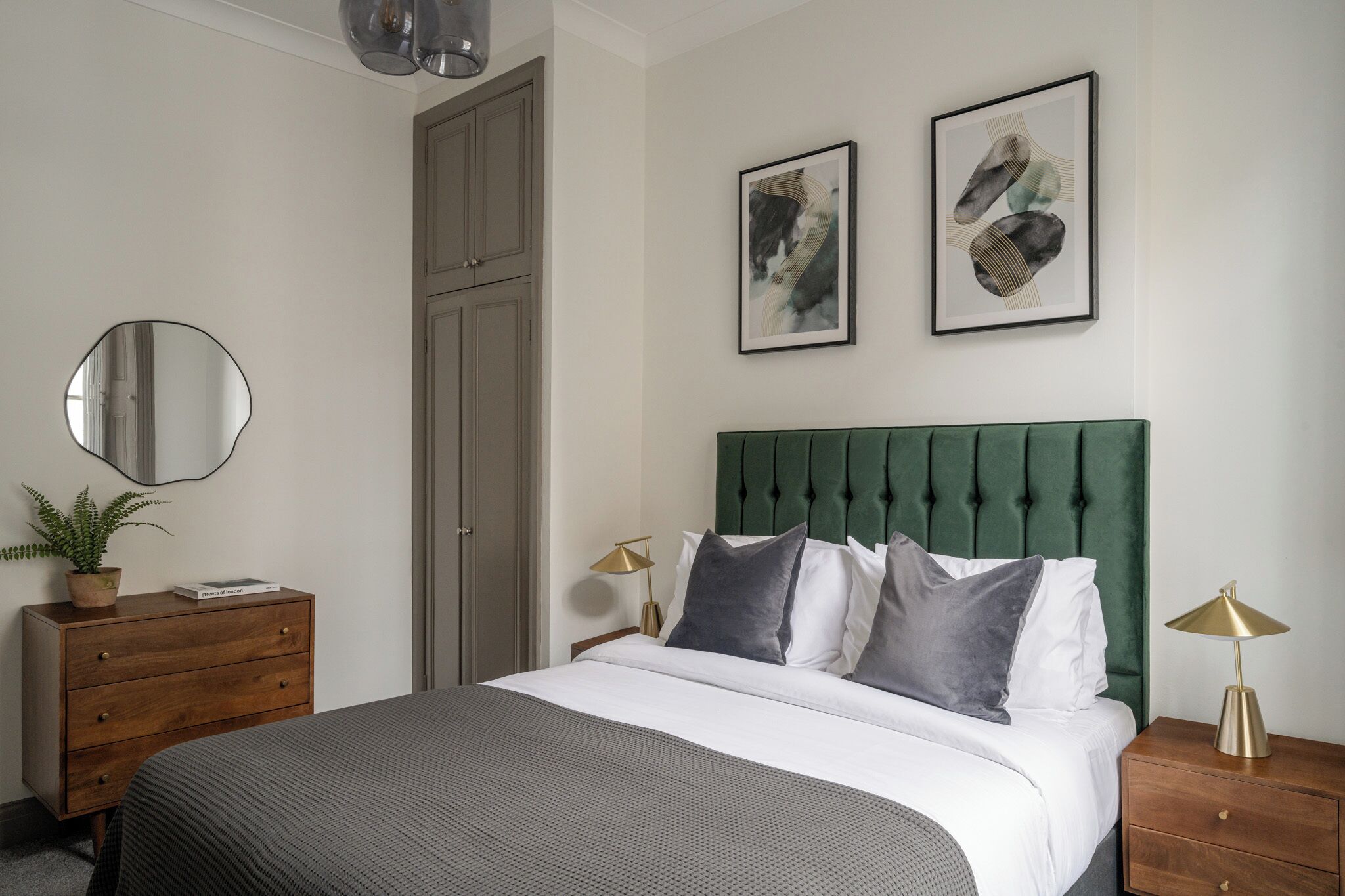 A neatly arranged bedroom with a bed, dresser, bedside lamps, and two framed artworks on the wall.