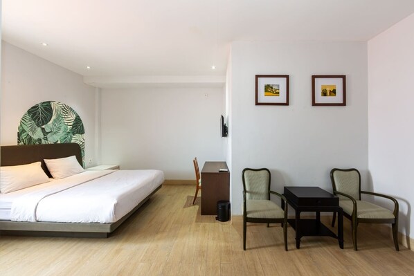 A hotel room with a bed, a desk, two chairs, and two framed pictures on the wall. - Cove Matahari Senja (Denpasar)