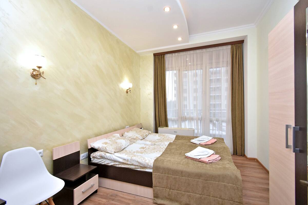 A bedroom with a bed, a desk, a chair, and a window with curtains.