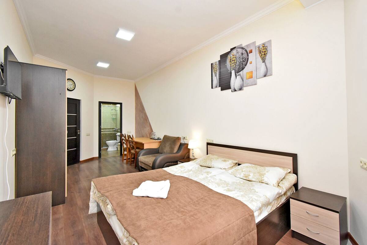 A hotel room with a bed, bedside table, desk, chair, and a bathroom visible through an open door.