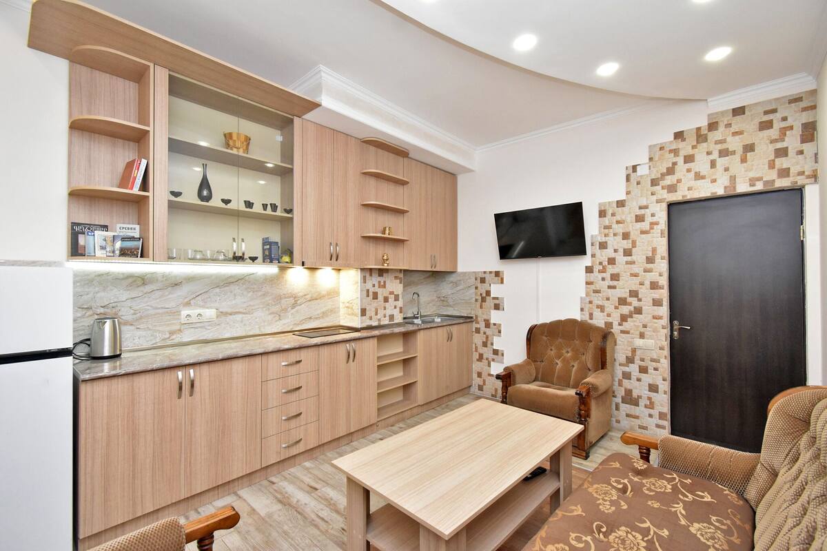 A modern kitchen with wooden cabinets, a marble countertop, and a built-in TV.