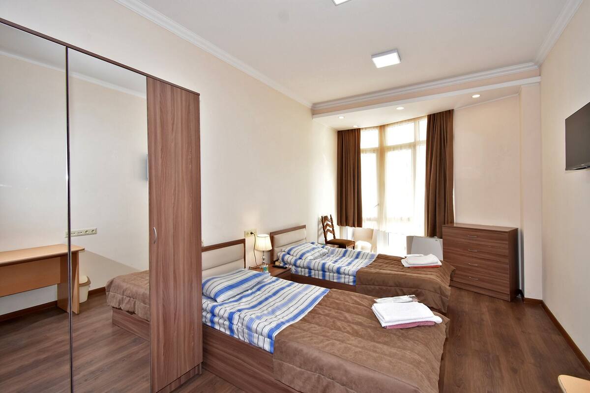 A hotel room with two beds, a desk, a mirror, a TV, and a wardrobe.