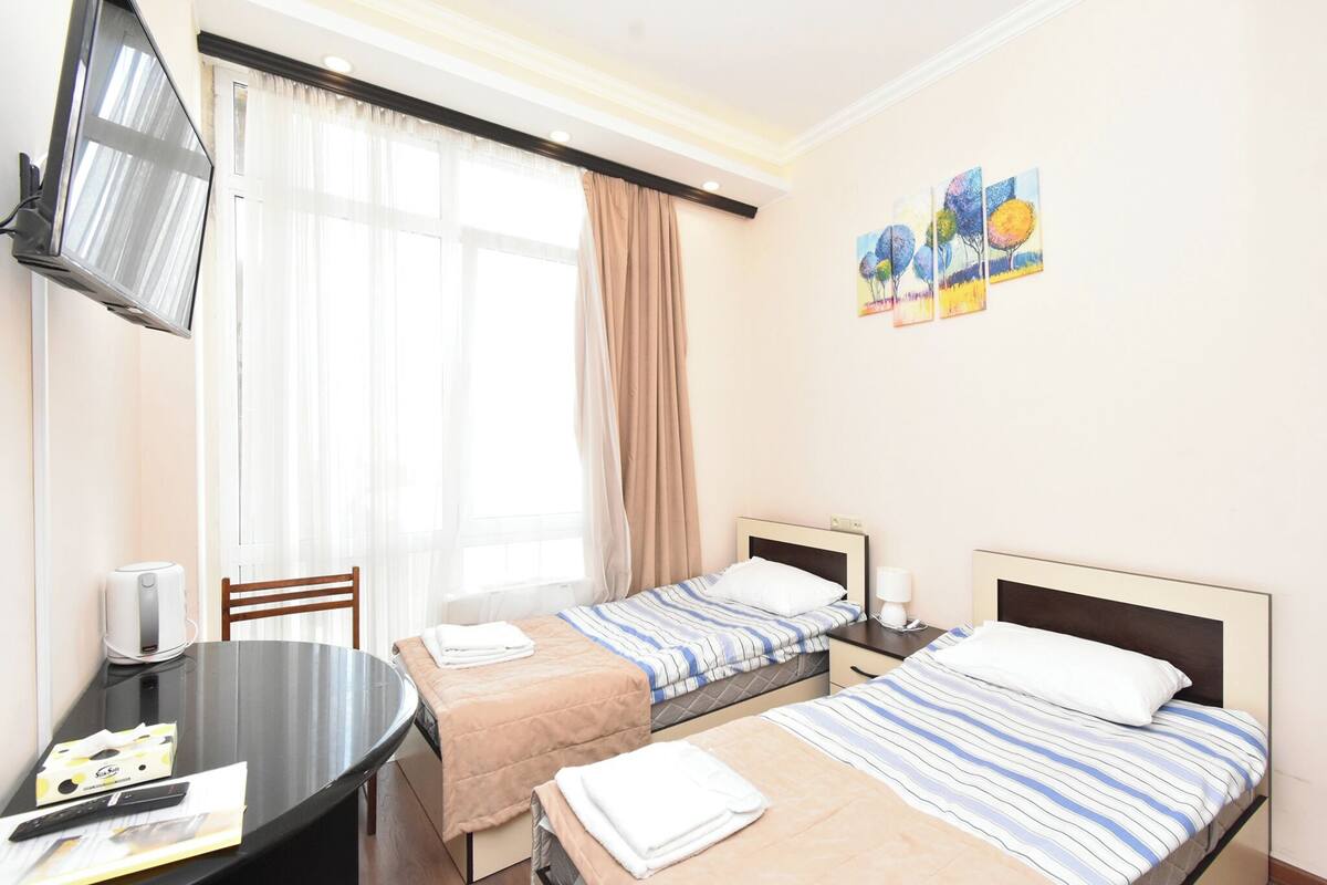 A hotel room with two beds, a TV, a table, and a window with curtains.