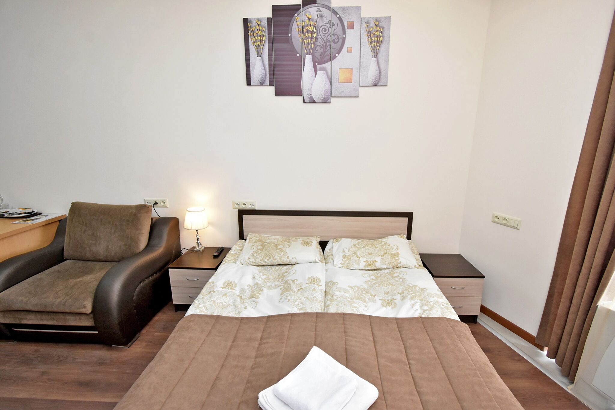 A hotel room with a bed, a sofa, a nightstand, a lamp, and a wall art piece.