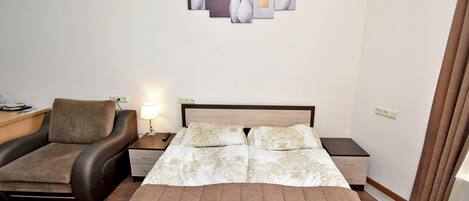 A hotel room with a bed, a sofa, a nightstand, a lamp, and a wall art piece.