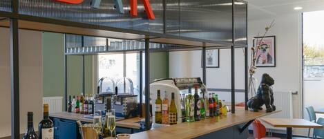 A bar area with a counter displaying various bottles and glasses, a coffee machine, and seating arrangements.