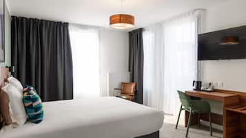A hotel room with a bed, a desk, a chair, a TV, and a window with curtains.
