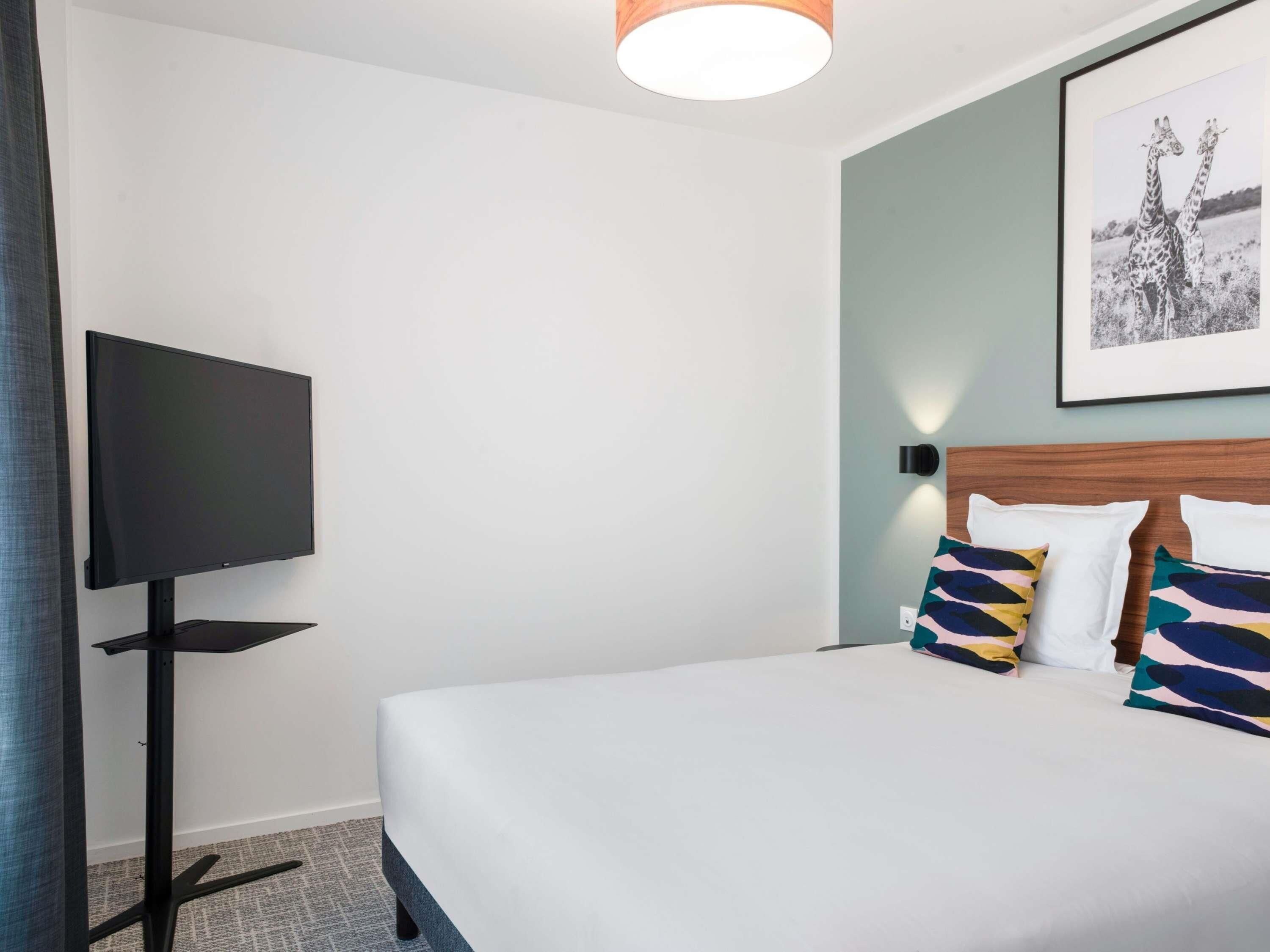 Une chambre d’hôtel avec un lit, un téléviseur à écran plat et un tableau encadré au mur.