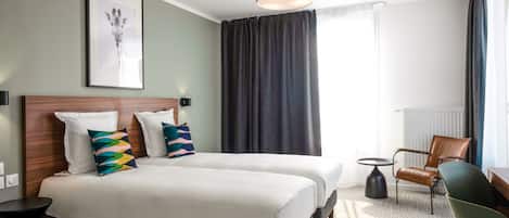 A hotel room with two beds, a desk, a chair, a lamp, and a framed picture on the wall.