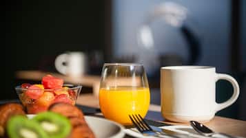 A breakfast setting with a glass of orange juice, a white mug, a plate with croissants and fruit, and breakfast utensils on a table.