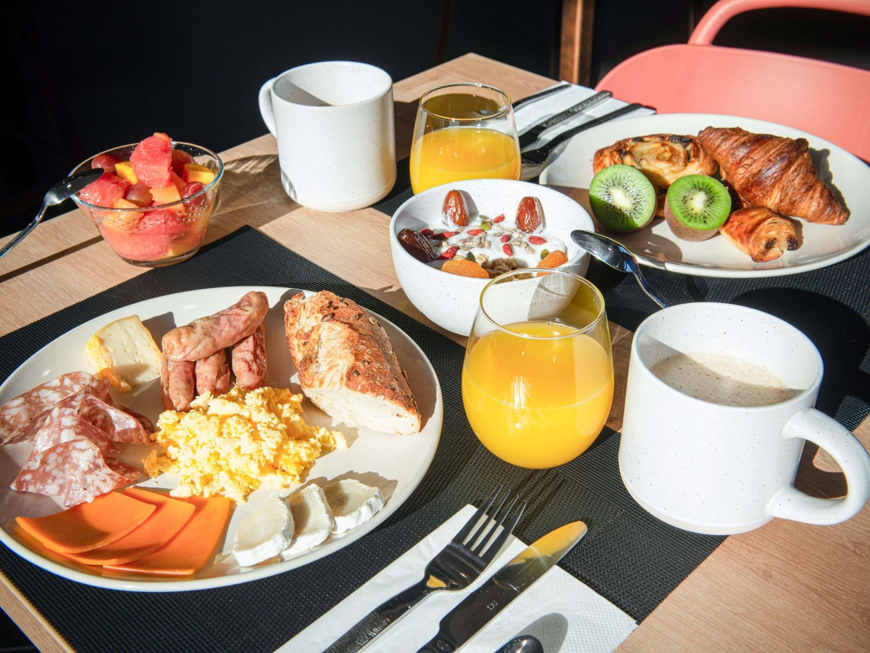 Ein Frühstückstisch mit Speisen, einer Obstschale, einem Glas Orangensaft und einem Croissant.
