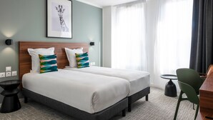 Habitación de hotel con dos camas, un escritorio, una silla, una mesita y un cuadro de una jirafa en la pared.