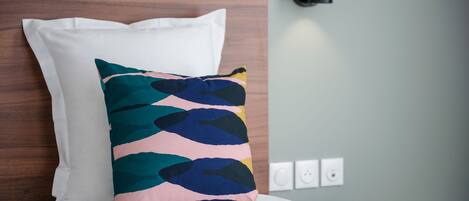 A bed with a white pillow and a colorful pillow, a wooden headboard, a black wall-mounted lamp, and a round table.