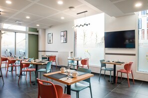 A modern cafe with multiple tables and chairs, a large TV screen, and framed artwork on the walls. - Aparthotel Adagio Access Lille Villeneuve-d'Ascq (Villeneuve-d'Ascq)