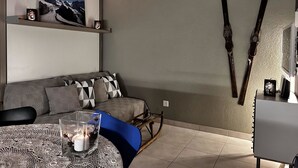 A modern living room with a grey sofa, a glass table with a candle, and skis mounted on the wall. - Evelyne by Interhome (Saas-Fee)
