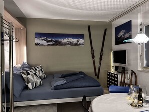 Ein gemütliches Schlafzimmer mit Bett, einem an der Wand befestigten Fernseher und einem Wandbild zum Thema Skifahren.