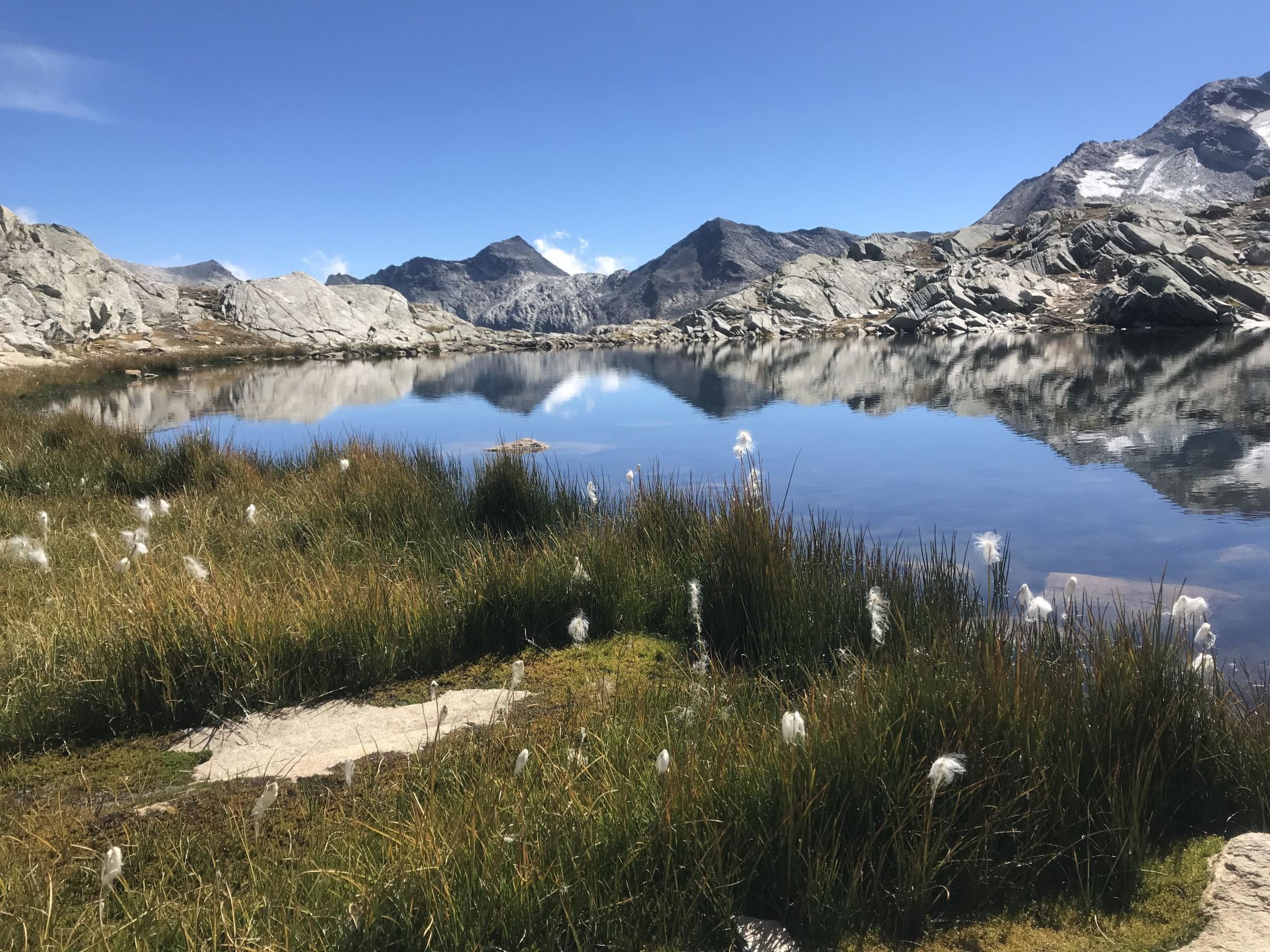 A serene mountain lake with clear reflections, surrounded by rocky terrain and sparse vegetation.