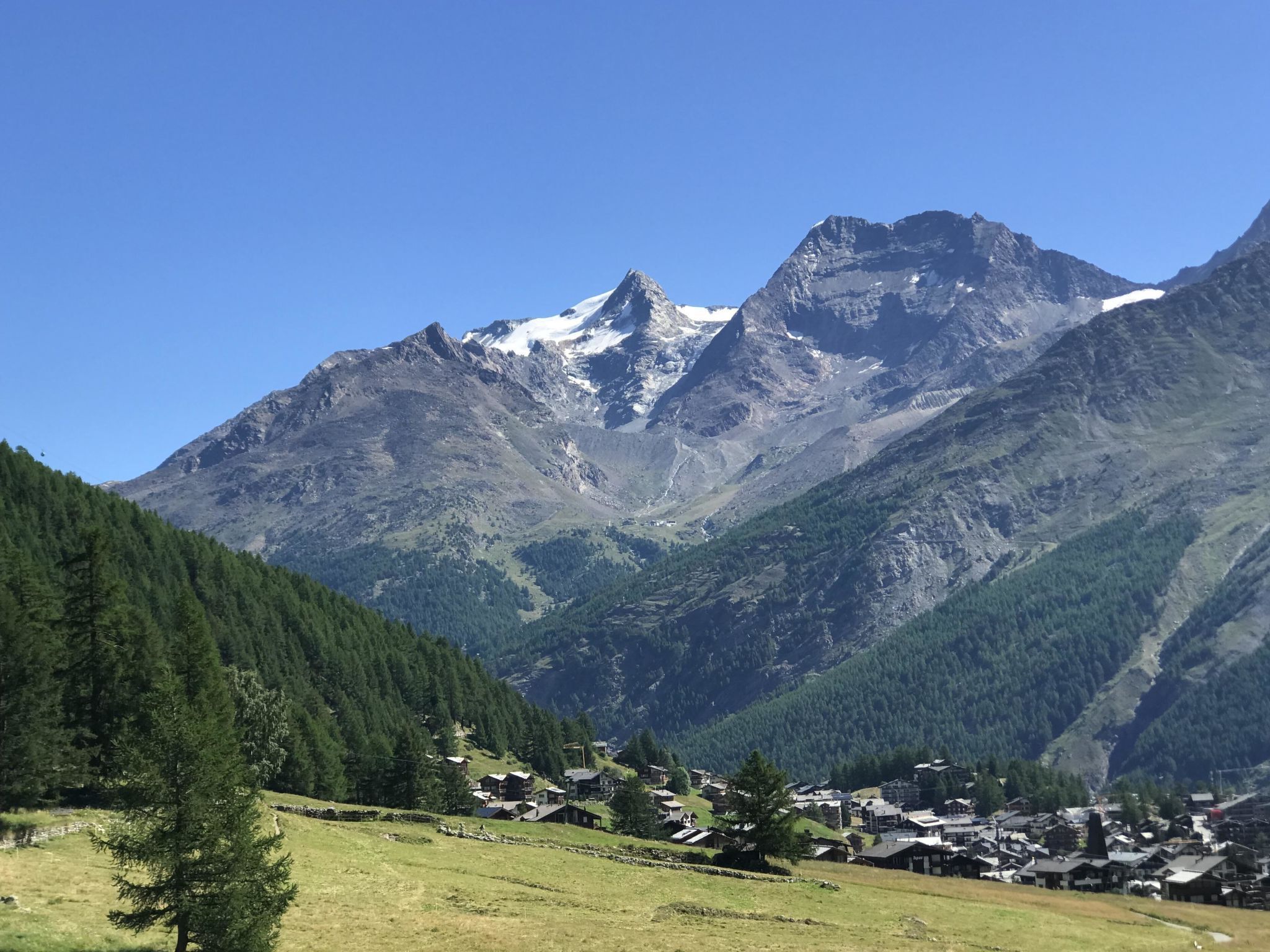 Un village de montagne aux maisons traditionnelles, avec un ciel dégagé et des sommets enneigés en toile de fond.