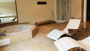 A modern bathroom with a large bathtub, a glass-enclosed shower, and two lounge chairs. - Evelyne by Interhome (Saas-Fee)
