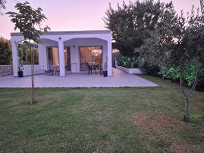 Ein modernes Haus mit überdachter Terrasse, einem Rasen und umgebender Bepflanzung.