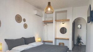 Une chambre moderne avec un grand lit, des lampes de chevet, des œuvres d’art décoratives au mur, un luminaire suspendu et un petit tabouret.