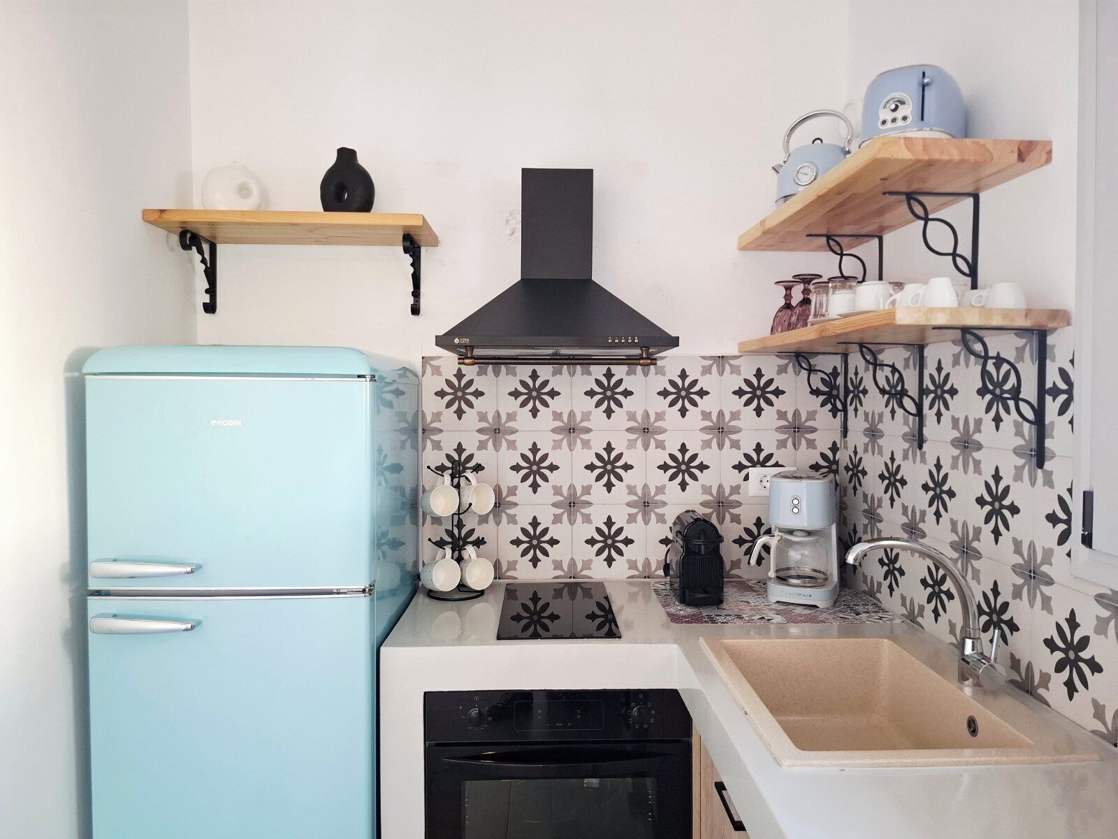 A compact kitchen with a light blue refrigerator, a black stove, a sink, and a coffee maker.