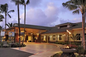 A hotel entrance with a curved driveway, palm trees, and a lit fire feature.
