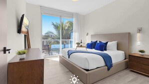 A modern bedroom with a large bed, a desk, and a balcony with a view of palm trees. - Amazing Pool+ Gym|Walk to Beach (Hollywood)