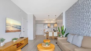 En moderne stue med sofa, sofabord og et spiseområde med et køkken i baggrunden.