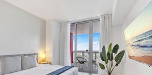 Una camera d'albergo con un letto, un comodino, una lampada, un balcone con una sedia e un'ampia finestra vista mare.