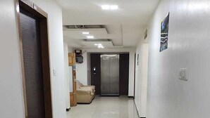 A clean, well-lit hallway with a tiled floor, a door on the left, and a sofa in the background. - Aayush Residency (Chennai)