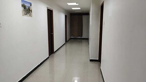 A long, narrow hallway with white walls and a tiled floor. - Aayush Residency (Chennai)