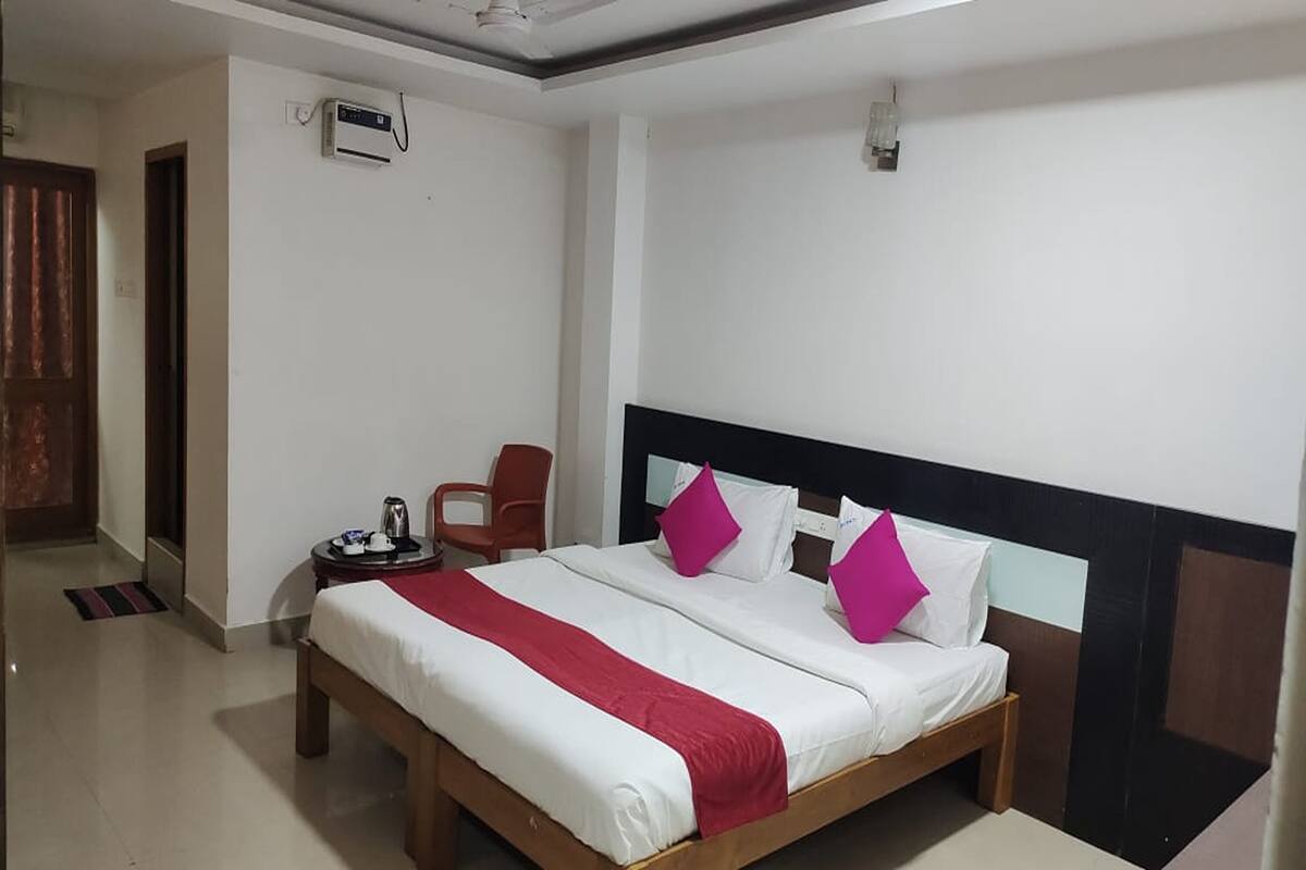 Habitación de hotel con cama, una silla, una mesita con hervidor y aire acondicionado instalado en la pared.
