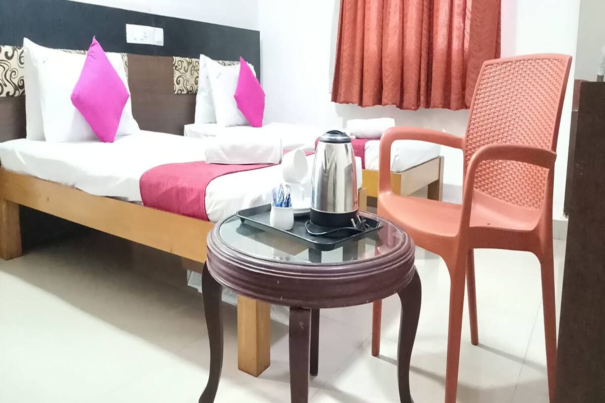 Habitación de hotel con cama, una mesa con hervidor, una silla y un ventanal con cortinas.
