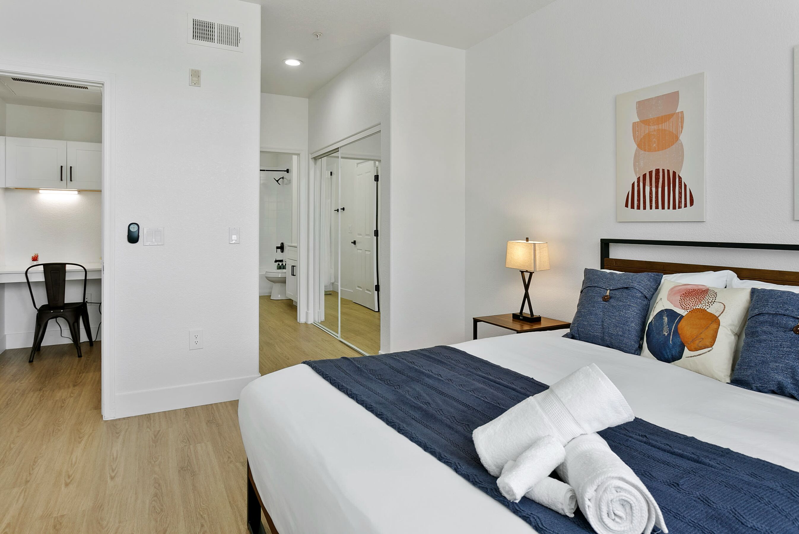 Una habitación de hotel con una cama bien hecha, un escritorio con una silla y un baño visible a través de una puerta abierta.
