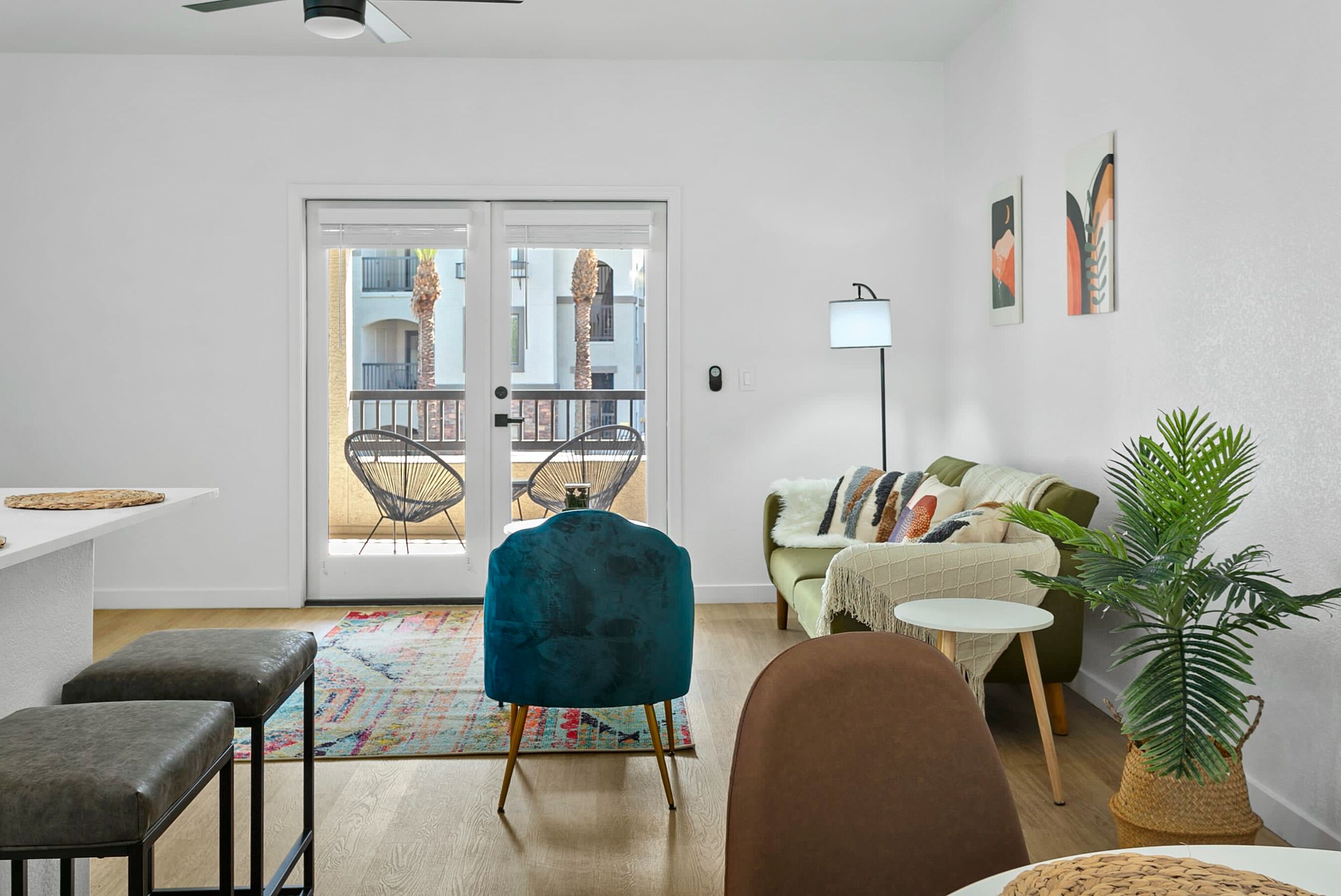 Una sala de estar moderna con una silla verde azulado, un sofá marrón y un sofá verde. Hay una pequeña mesa y una planta en la esquina.